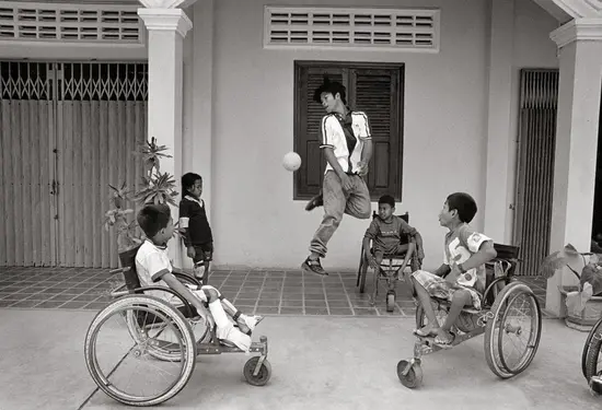 Sokheurm Man, mutilado por una mina, juega ante un grupo de niños poliomielíticos. Battambang (Camboya), abril de 2002